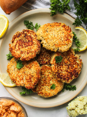 zoomed out shot of salmon sweet potato cakes on a grey ceramic plate topped with fresh parsley and ingredients surrounding the plate