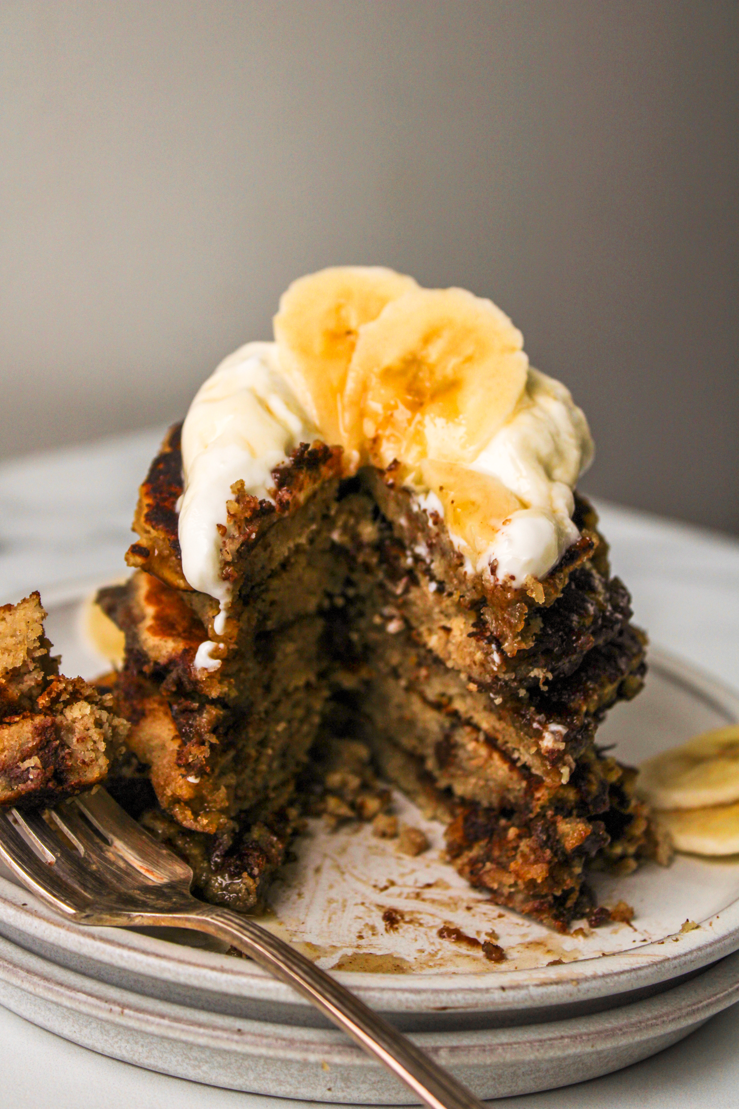 cut pancakes stacked on top of a white plate and topped with greek yogurt, banana and maple syrup