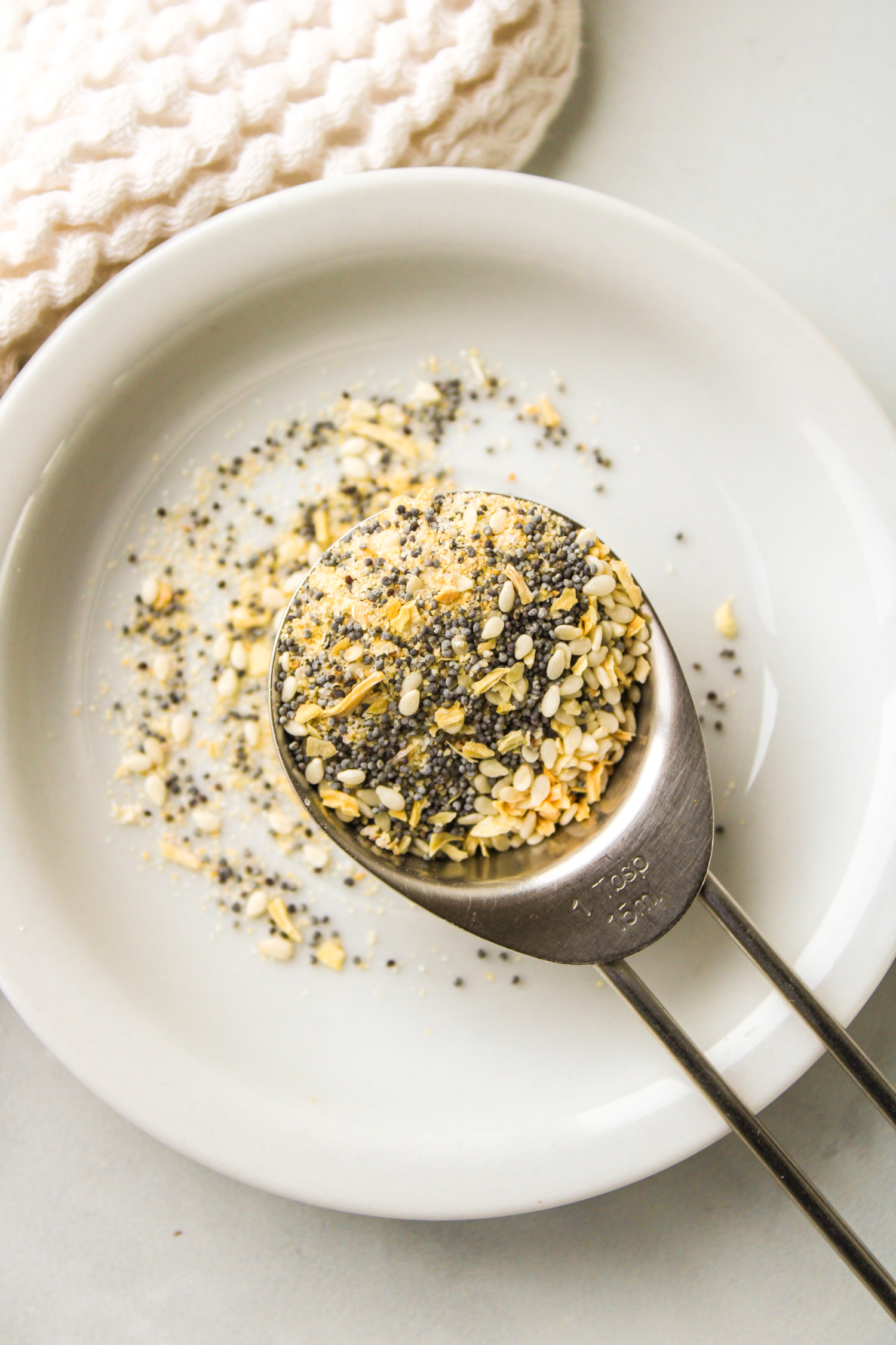 everything but the bagel seasoning in a metal measuring spoon on top of a small white plate