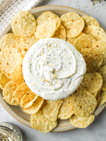 overhead shot of everything but the bagel dip in a white bowl surrounded by corn chips
