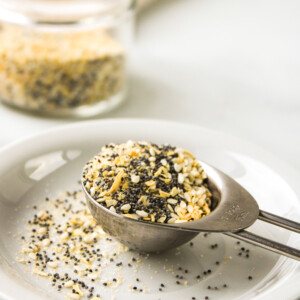 profile shot of everything but the bagel seasoning in a metal measuring spoon on top of a small white plate