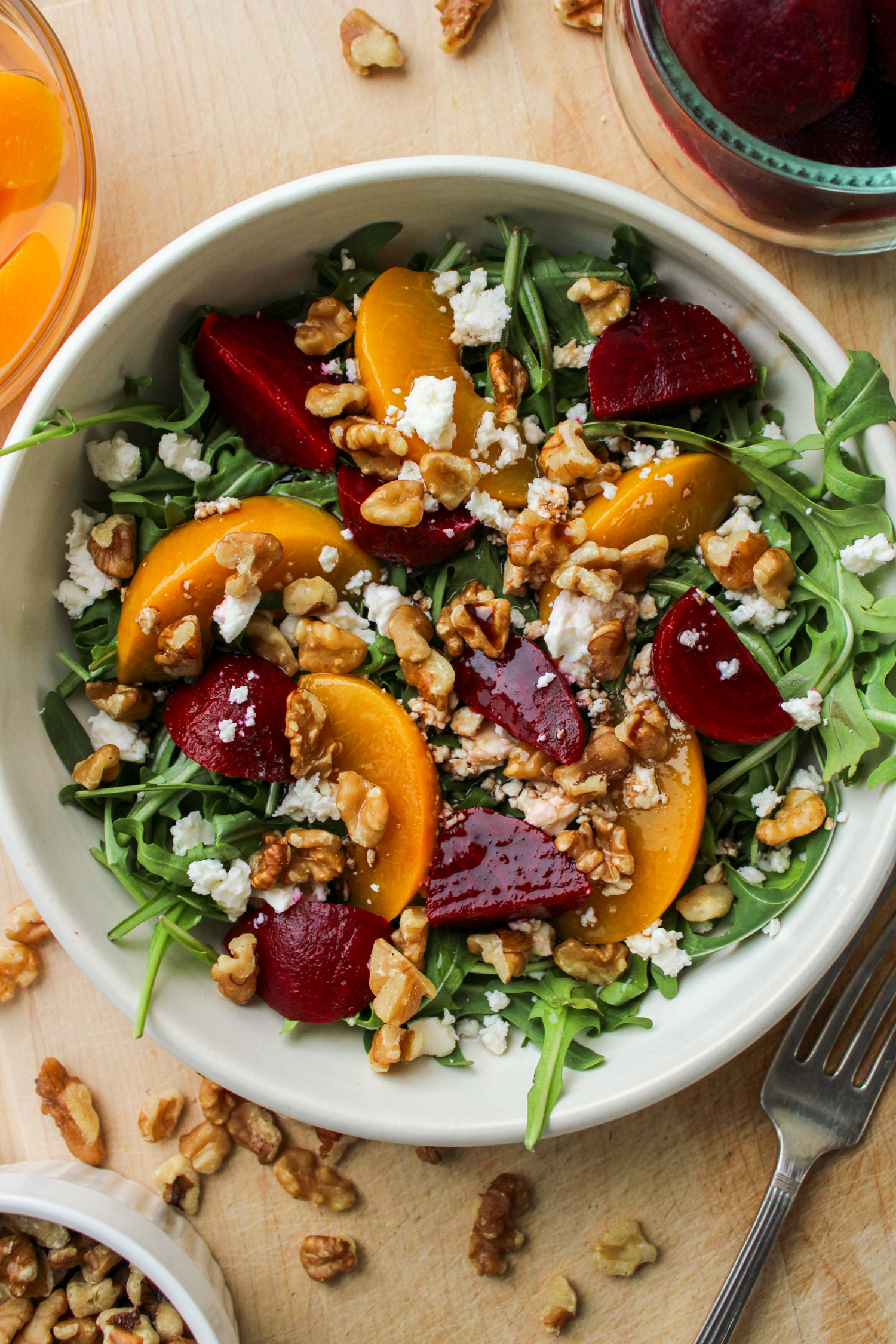 overhead shot of beetroot salad with walnuts and feta in a cream ceramic bowl on top of a wooden board