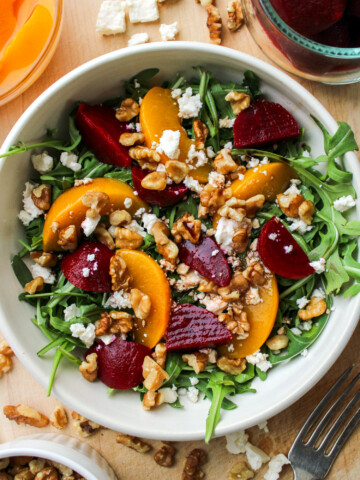 beetroot salad with walnuts and feta in a cream ceramic bowl on top of a wooden board