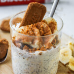 overnight oats topped with banana, cinnamon and a biscoff cookie sticking out of it, all in a glass container