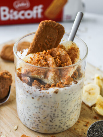 overnight oats topped with banana, cinnamon and a biscoff cookie sticking out of it, all in a glass container