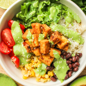 overhead shot of tofu burrito bowl with avocado cilantro sauce drizzled on top in a white ceramic dish