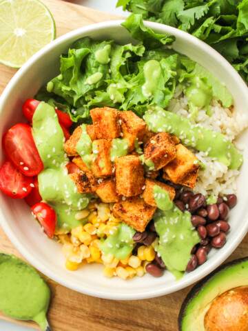 overhead shot of tofu burrito bowl with avocado cilantro sauce drizzled on top in a white ceramic dish