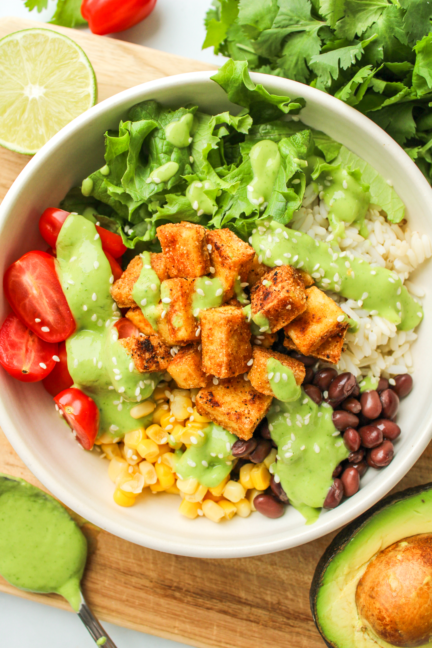 overhead shot of tofu burrito bowl with avocado cilantro sauce drizzled on top in a white ceramic dish