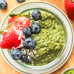 matcha chia seed pudding in a small glass bowl topped with berries and coconut flakes on top of a wooden board