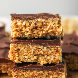 3 squares of cashew bar with chocolate coating stacked on top of each other, profile shot