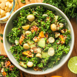 parsley quinoa salad with mango in a white ceramic bowl on top of a wooden cutting board surrounded with ingredients used