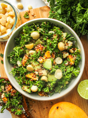 parsley quinoa salad with mango in a white ceramic bowl on top of a wooden cutting board surrounded with ingredients used