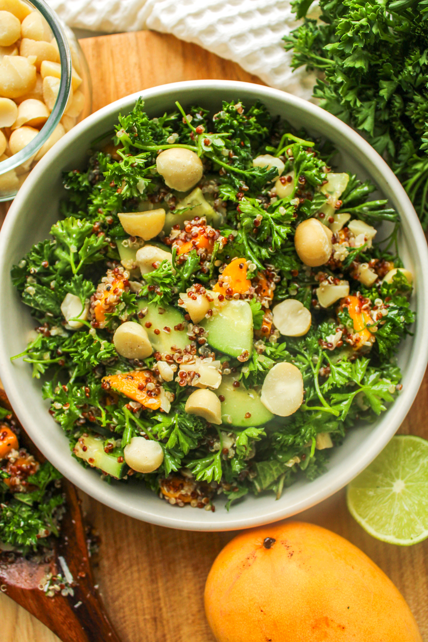 close up of salad in a white ceramic bowl on top of a wooden cutting board surrounded with ingredients used
