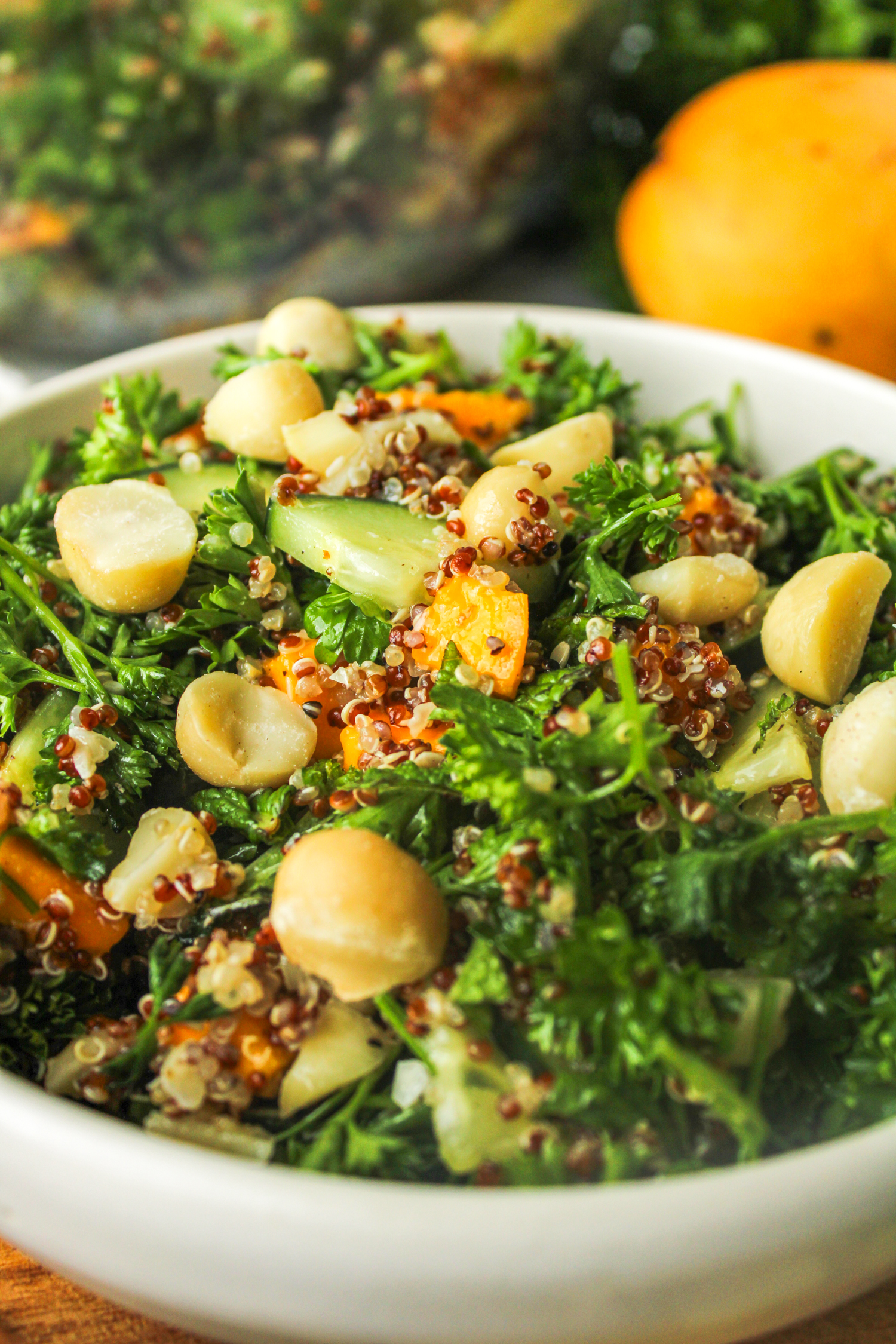 close up side profile of salad in a white ceramic bowl on top of a wooden cutting board surrounded with ingredients used