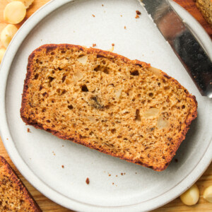 slice of macadamia banana bread on a grey ceramic plate on top of a wooden cutting board
