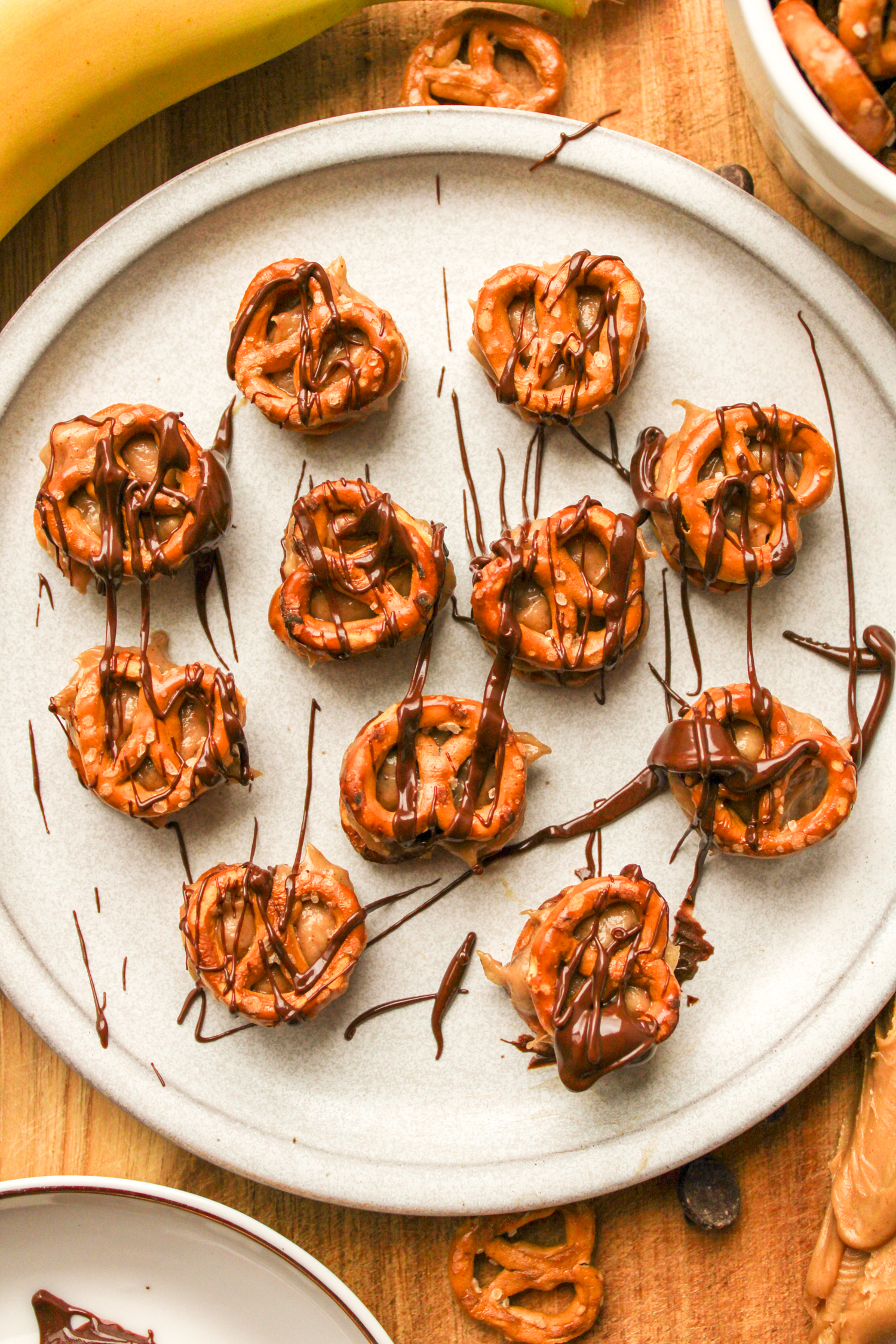pretzel peanut butter bites drizzled with chocolate on a grey ceramic plate, surrounded by recipe ingredients