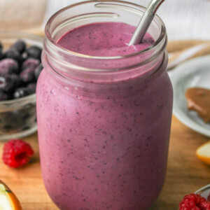 angled overhead shot of raspberry blueberry smoothie in a glass mason jar with a metal straw on top of a wooden board