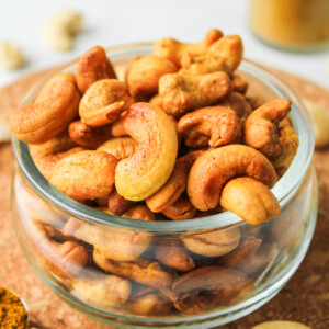 roasted curry cashews in a glass bowl on top of a cork hot pad