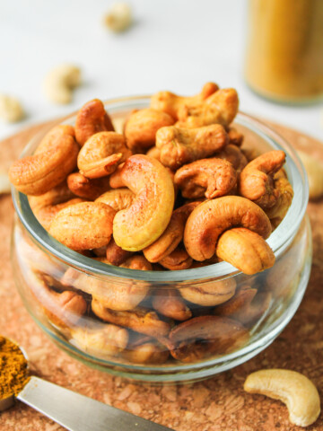 roasted curry cashews in a glass bowl on top of a cork hot pad