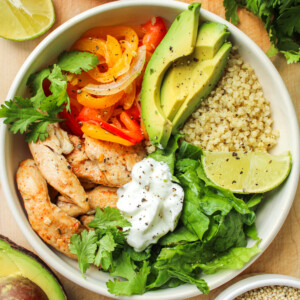 chicken quinoa bowls in a white ceramic dish on top of a wooden cutting board