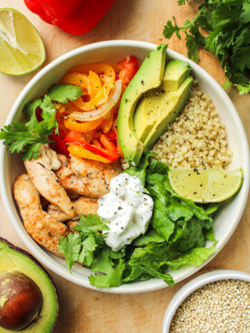 chicken quinoa bowls in a white ceramic dish on top of a wooden cutting board