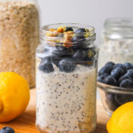 lemon blueberry overnight oats in a glass jar topped with fresh blueberries and lemon zest, on top of a wooden board