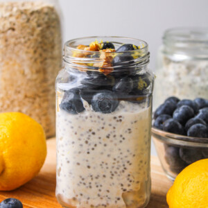 lemon blueberry overnight oats in a glass jar topped with fresh blueberries and lemon zest, on top of a wooden board