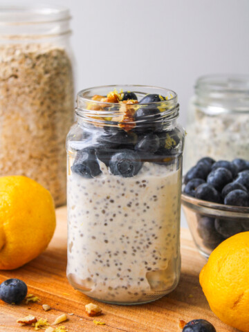 lemon blueberry overnight oats in a glass jar topped with fresh blueberries and lemon zest, on top of a wooden board