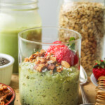 matcha overnight oats in a glass jar topped with strawberries and granola on top of a wooden cutting board