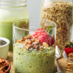 matcha overnight oats in a glass jar topped with strawberries and granola on top of a wooden cutting board