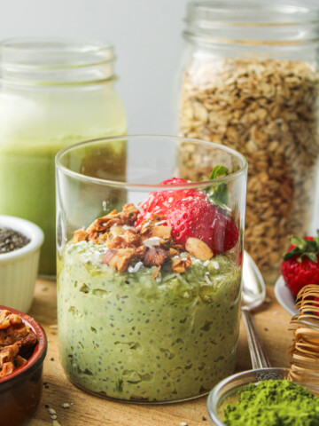 matcha overnight oats in a glass jar topped with strawberries and granola on top of a wooden cutting board