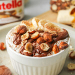 nutella overnight oats in a white ceramic dish topped with nutella, sliced banana, chopped hazelnuts and cocoa powder