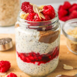 raspberry overnight oats layered in a glass jar topped with raspberries and sliced almonds