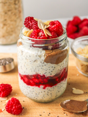 raspberry overnight oats layered in a glass jar topped with raspberries and sliced almonds