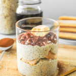 tiramisu overnight oats topped with cocoa powder and a ladyfinger cookie in glass jar on top of wooden board