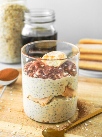 tiramisu overnight oats topped with cocoa powder and a ladyfinger cookie in glass jar on top of wooden board