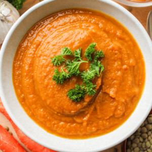 butternut squash and carrot soup topped with green parsley, in a white ceramic bowl on top of a wooden cutting board