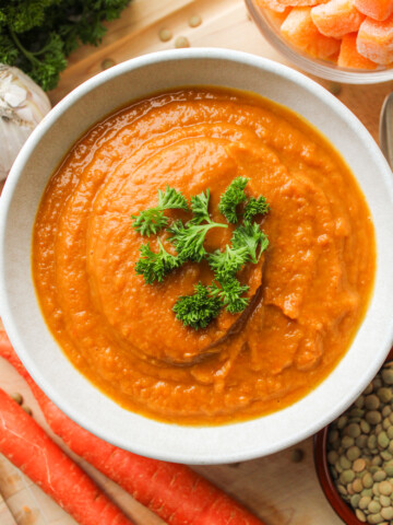 butternut squash and carrot soup topped with green parsley, in a white ceramic bowl on top of a wooden cutting board
