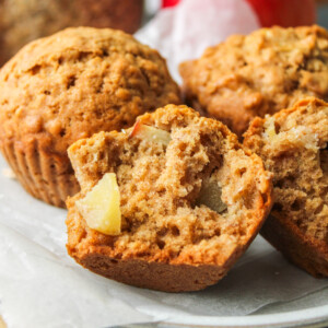 half an healthy apple oatmeal muffins on stacked white ceramic plates with other muffins surrounding it