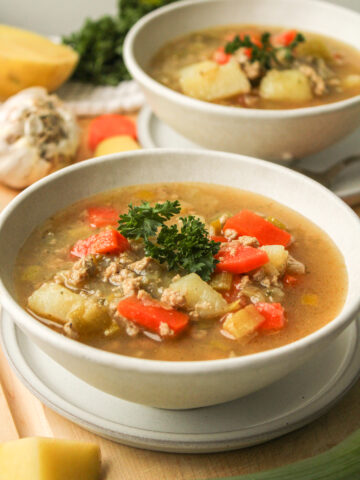 profile shot of potato leek soup with chicken topped with fresh parsley in a white ceramic bowl with another bowl of soup in the background