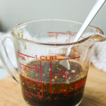maple balsamic dressing in a glass measuring cup on a wooden cutting board