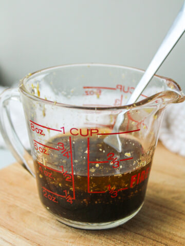 maple balsamic dressing in a glass measuring cup on a wooden cutting board