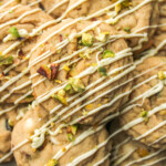 pistachio chocolate chip cookies layered on top of each other, drizzled in white chocolate and crumbled pistachios on top