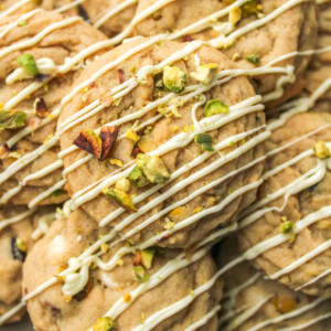 pistachio chocolate chip cookies layered on top of each other, drizzled in white chocolate and crumbled pistachios on top
