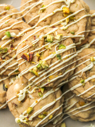 pistachio chocolate chip cookies layered on top of each other, drizzled in white chocolate and crumbled pistachios on top