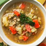 overhead shot of potato leek soup with chicken topped with fresh parsley in a white ceramic bowl with fresh ingredients surrounding it