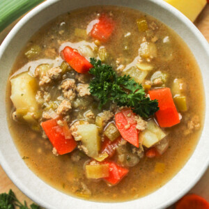 overhead shot of potato leek soup with chicken topped with fresh parsley in a white ceramic bowl with fresh ingredients surrounding it