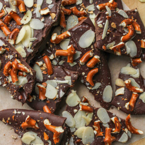 pretzel almond bark pieces on top of a wooden cutting board with pieces of pretzels, almonds and chocolate around the bark