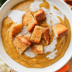 carrot and lentil soup with garlic bread bites in a white ceramic bowl on a wooden board