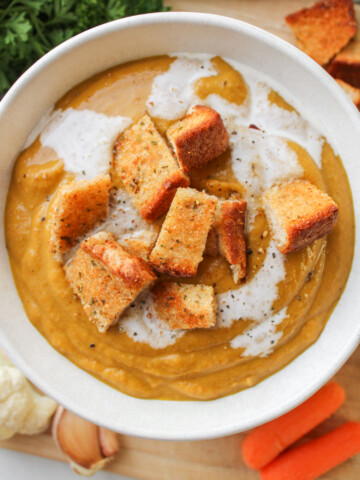carrot and lentil soup with garlic bread bites in a white ceramic bowl on a wooden board